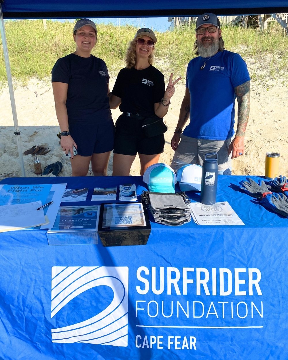 Sam poses with two volunteers under a blue Surfrider tent.