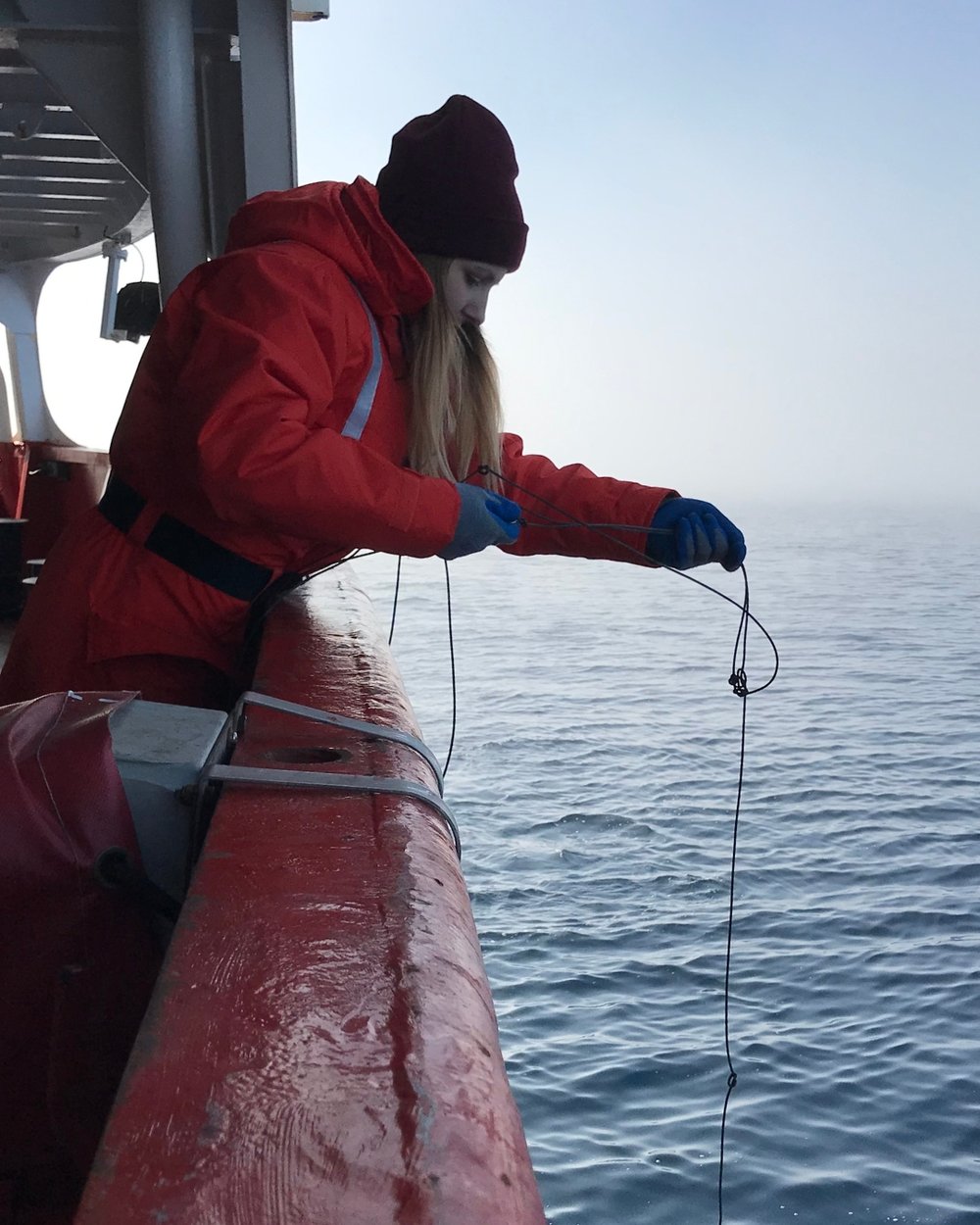 Sam reaches over the edge of a boat, testing water samples.