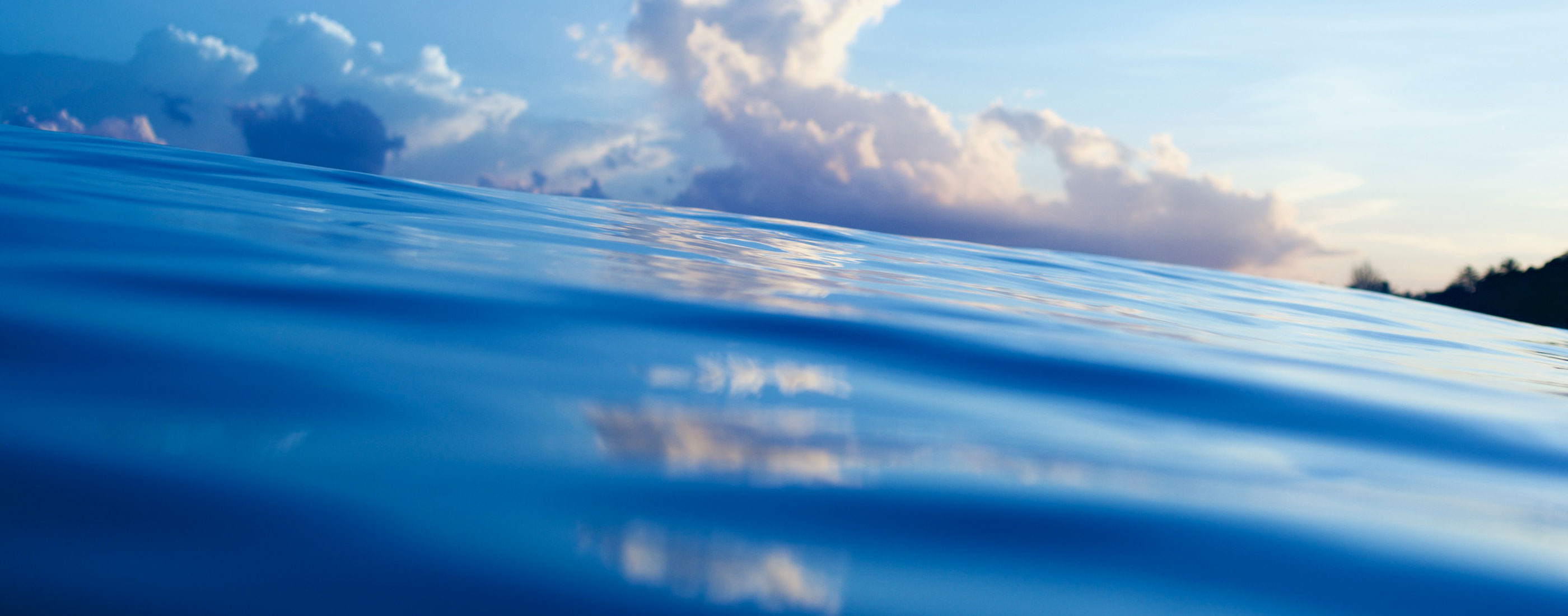 An eye level view of a body of water with white clouds in a mostly sunny sky